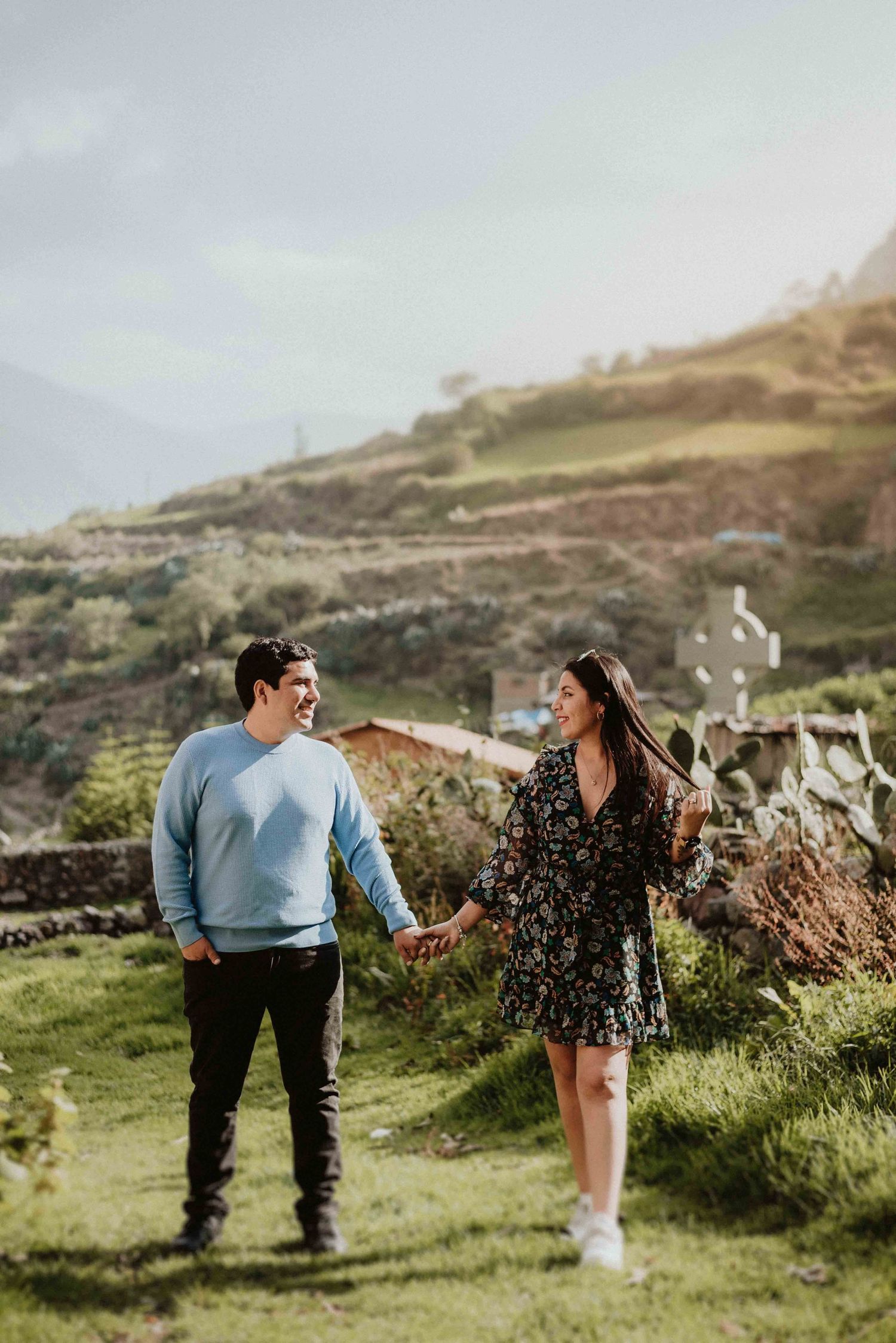 A couple holding hands while exploring green hillsides on a cloudy day in the countryside.