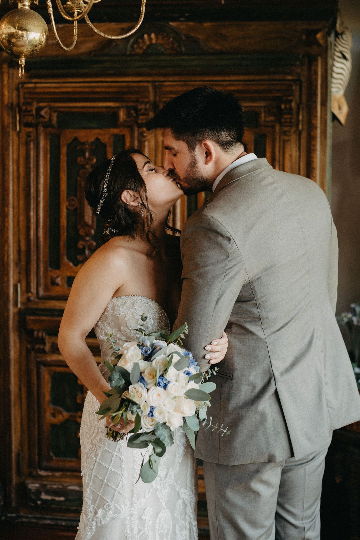 Romantic wedding portrait in front of ornate wooden door with white and blue floral bouquet.