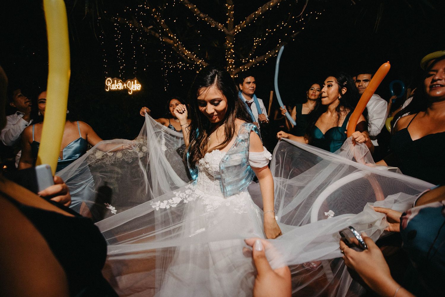 Wedding celebration with guests playing with the bride's veil on a dance floor.
