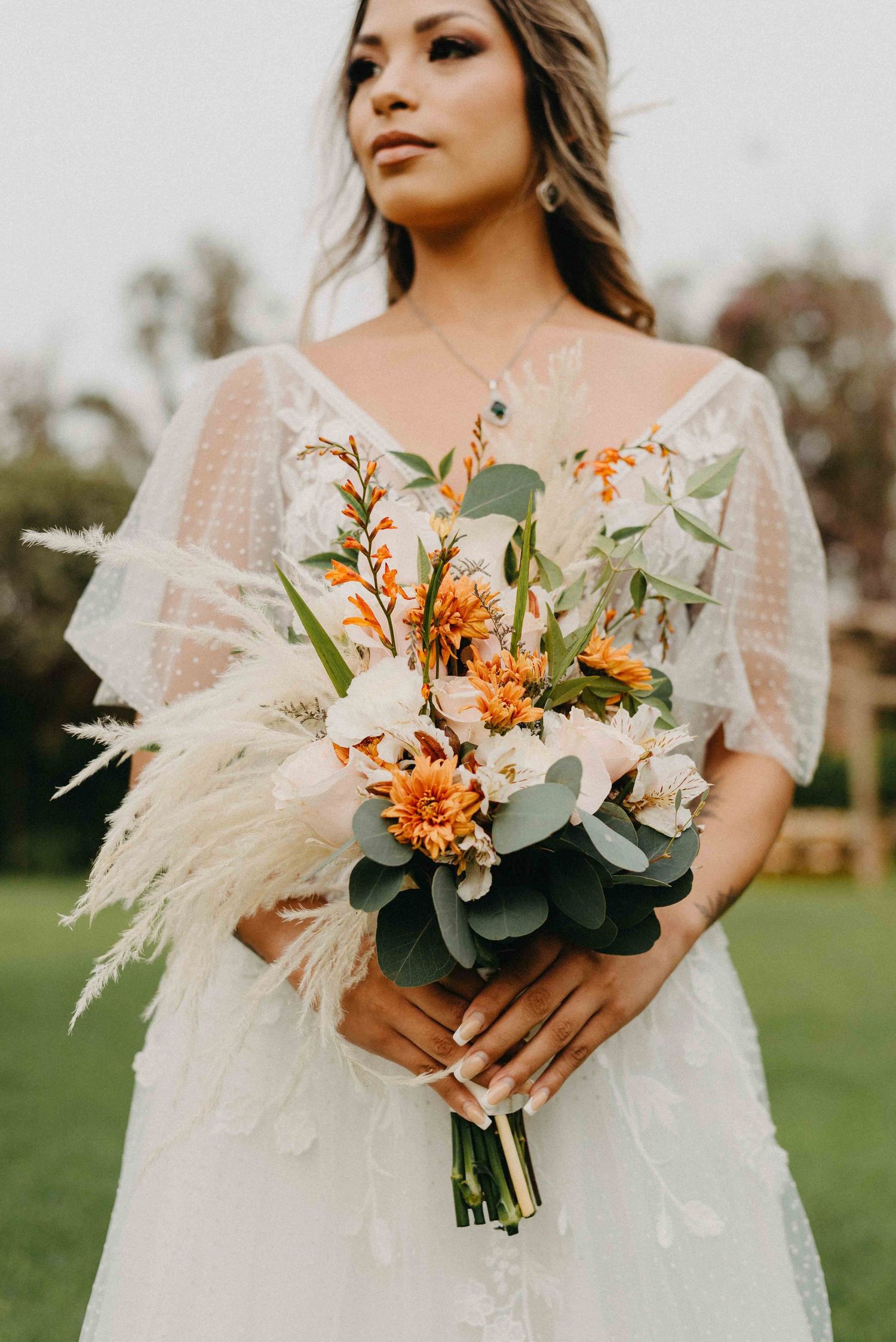 Bride holds a stunning autumn-inspired bouquet with orange flowers and pampas grass accents.