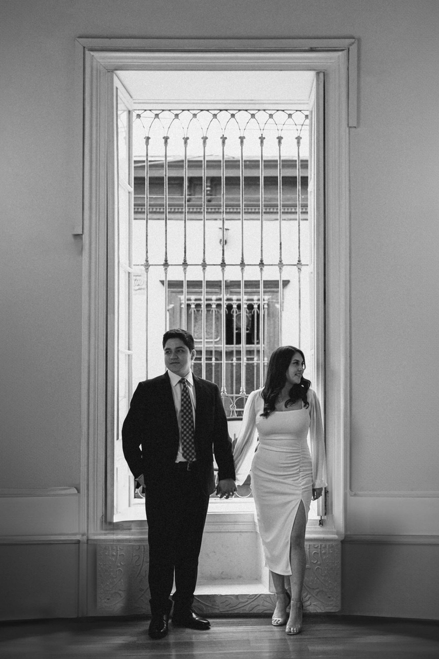Black and white wedding photos showing couple walking through elegant hallway with ornate windows.