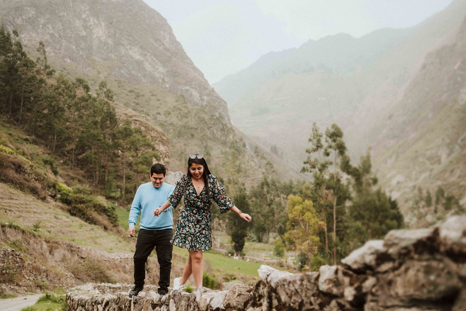 A couple enjoying a scenic moment together while hiking on a mountain trail surrounded by peaks.