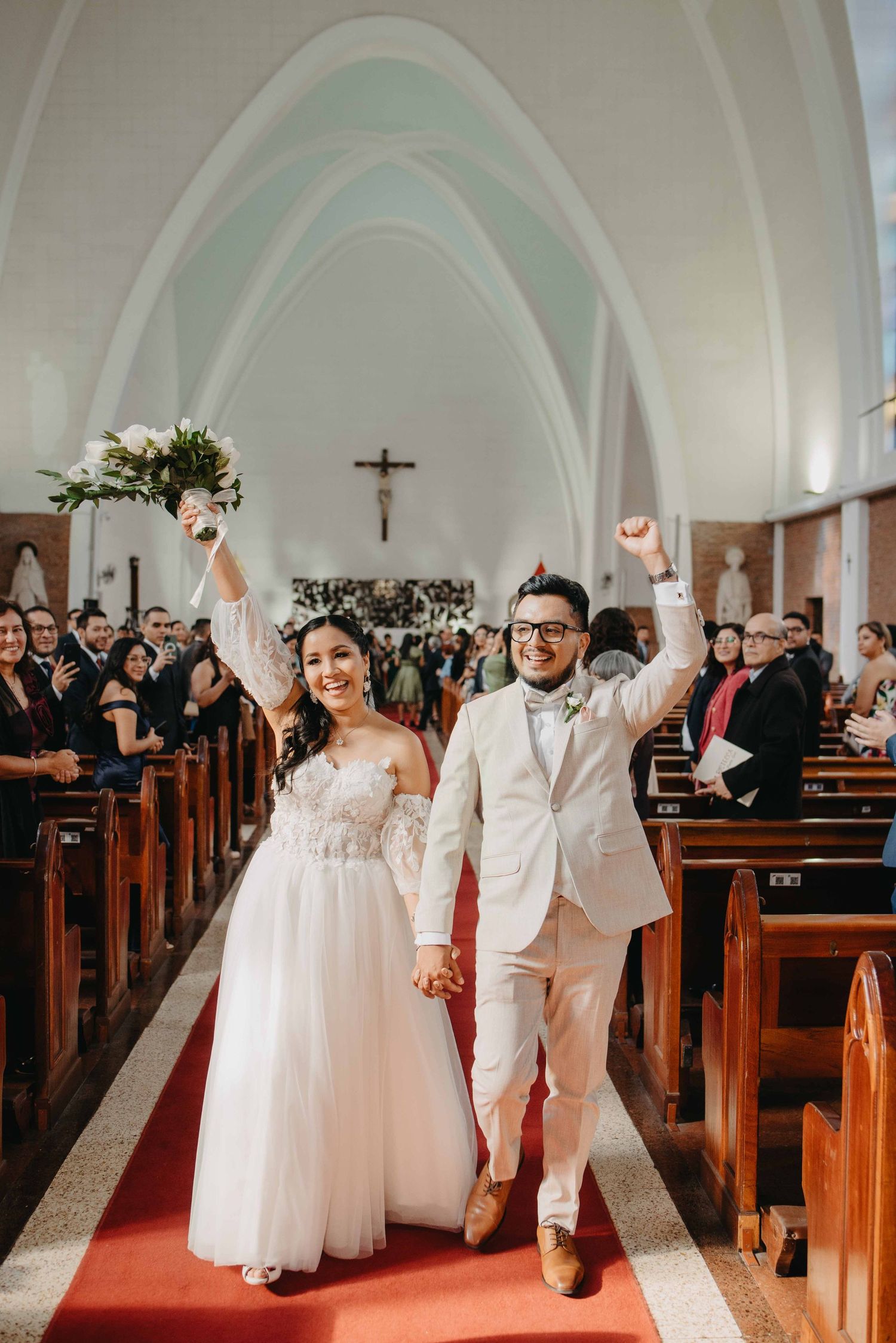 A joyful celebration in a church as newlyweds walk down the aisle with raised arms amid wooden pews.