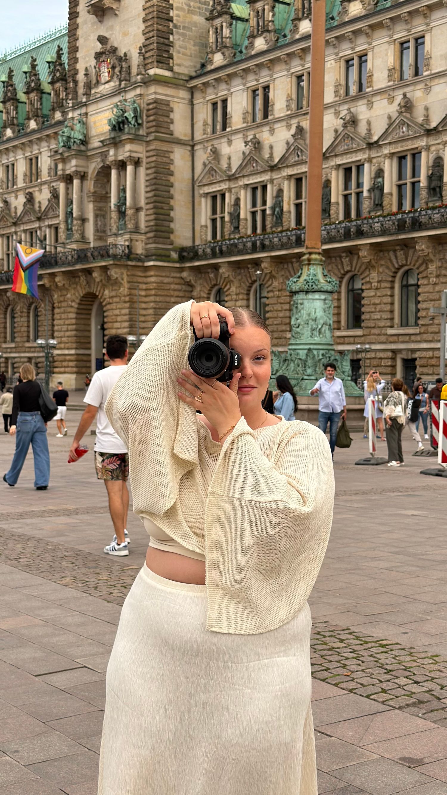 Woman in white outfit photographing with camera at Hamburg City Hall.