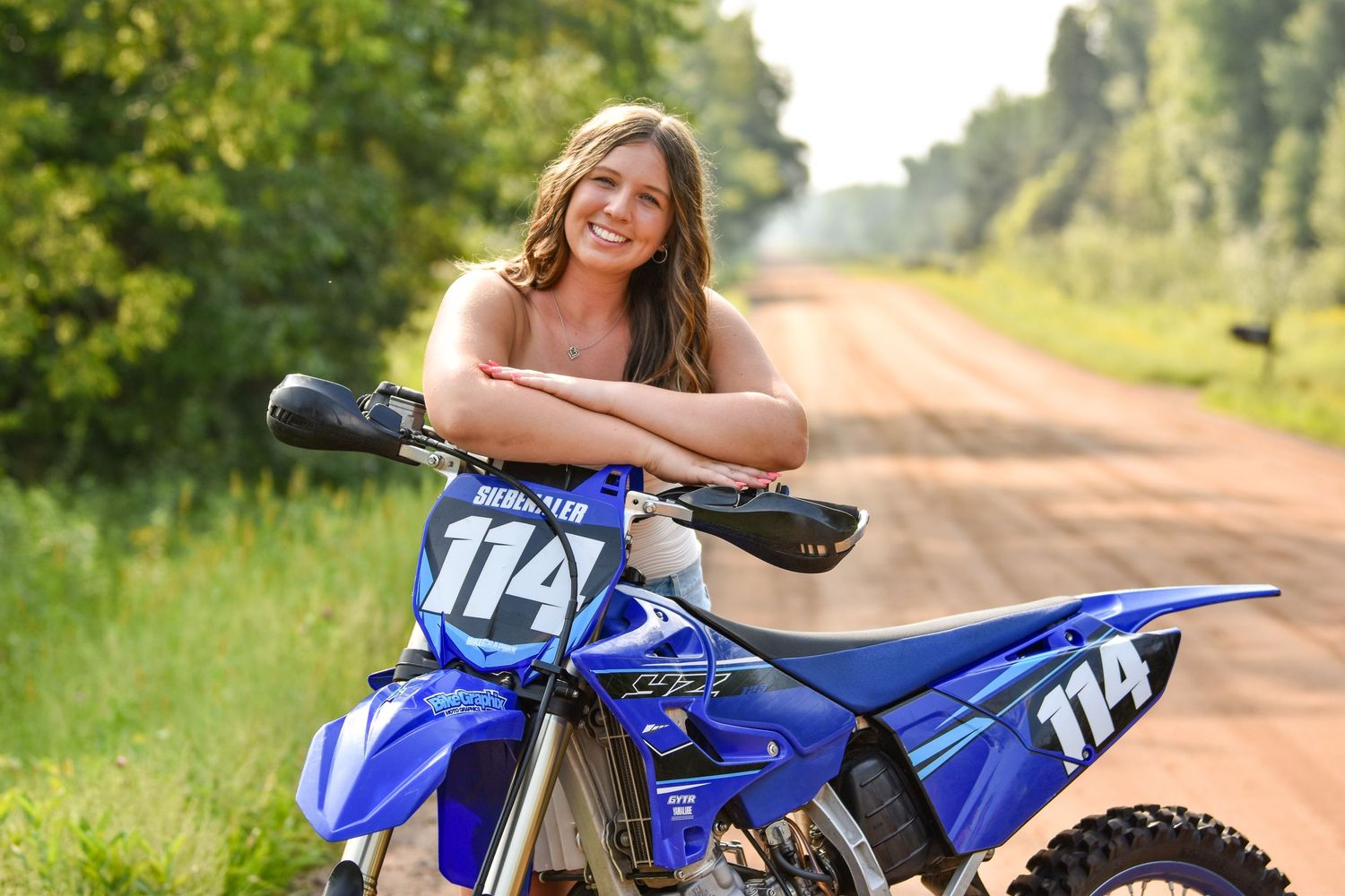 Blue Yamaha dirt bike parked on a rural dirt road with green foliage in the background.