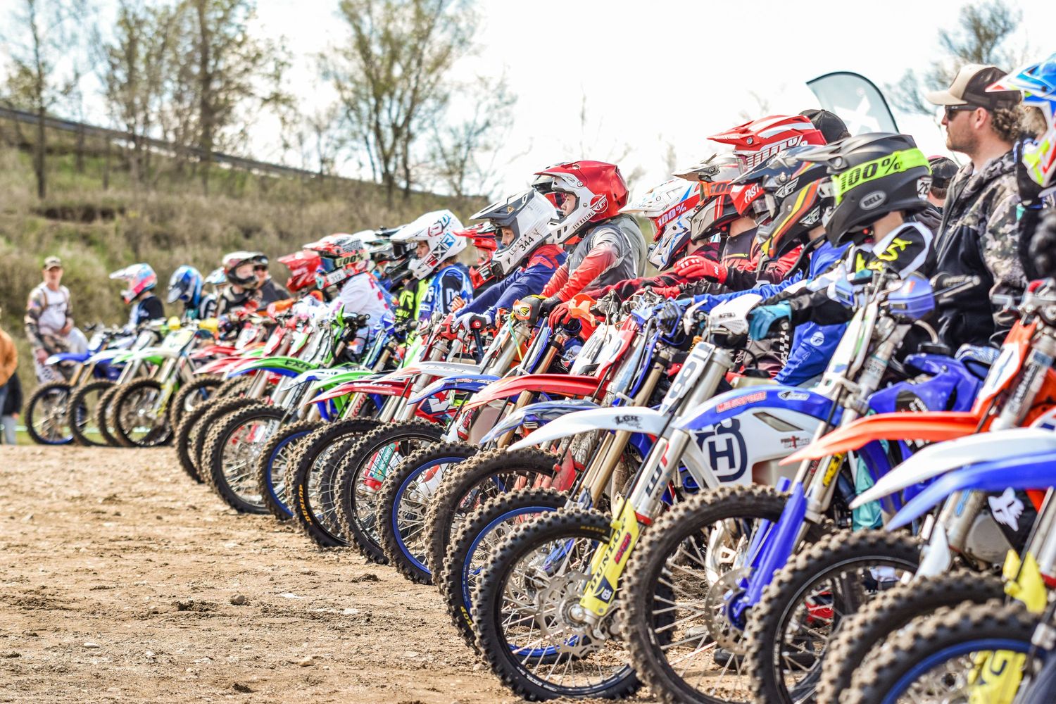 Row of motocross bikes lined up at outdoor racing event showing various brands and colors.