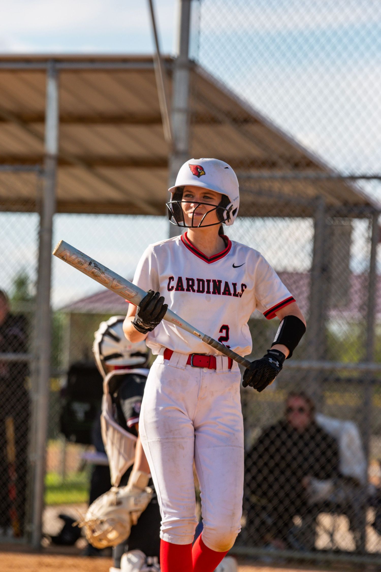 Softball player in white Cardinals uniform takes batting stance at home plate.