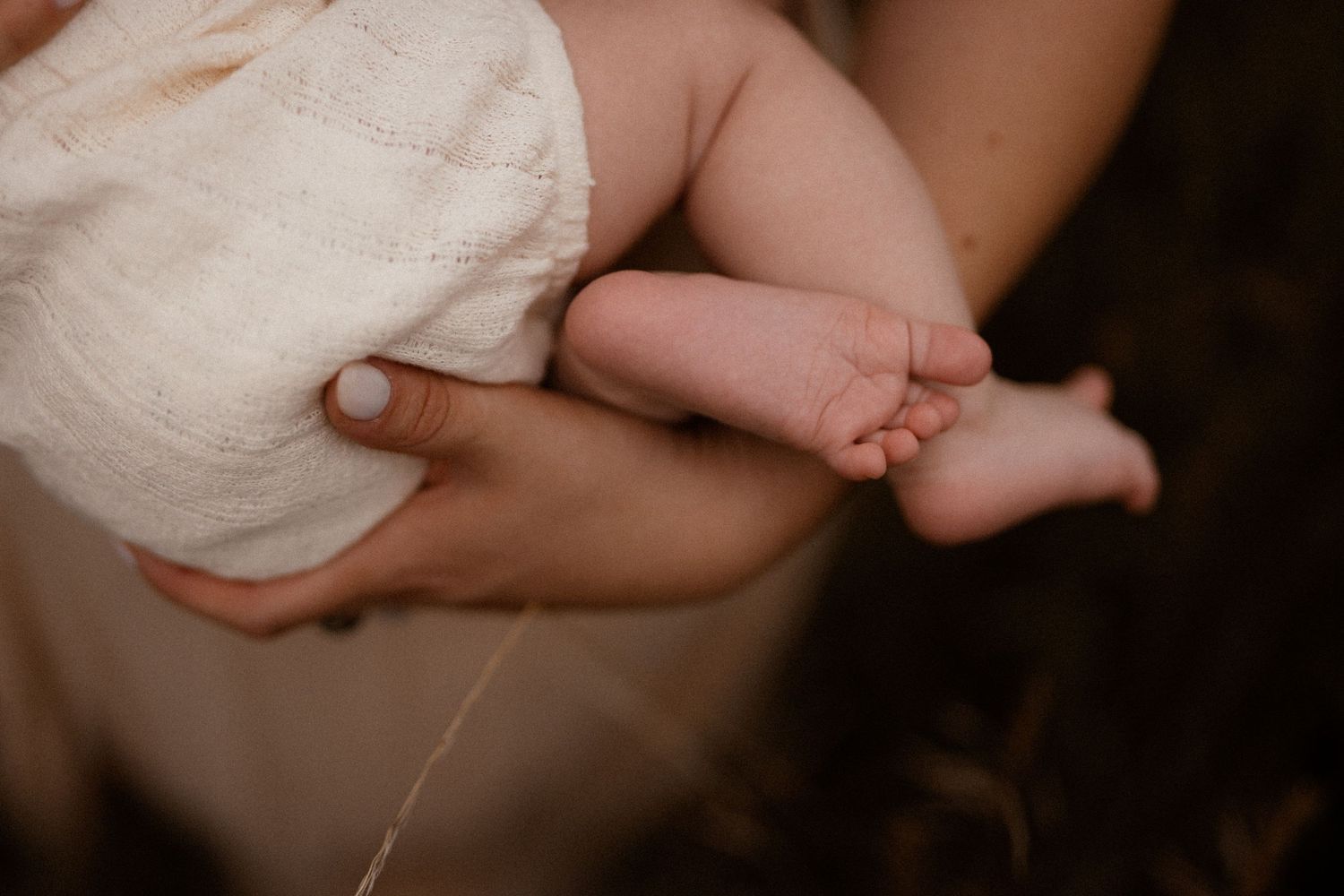 A tiny baby foot is gently cradled in someone's hands against a white cloth background.