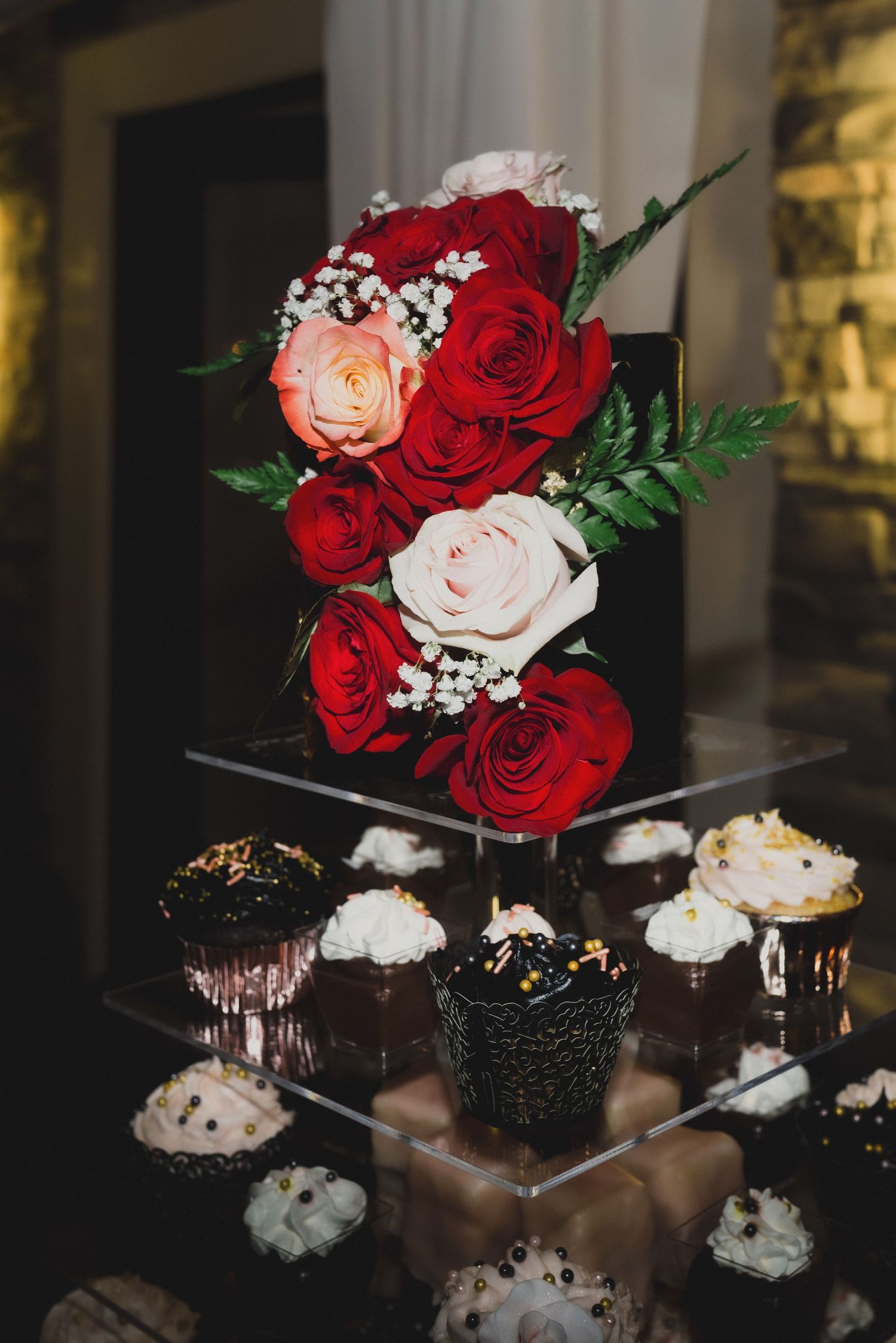Elegant floral arrangement of red and pink roses displayed above chocolate cupcakes on tiered stand.