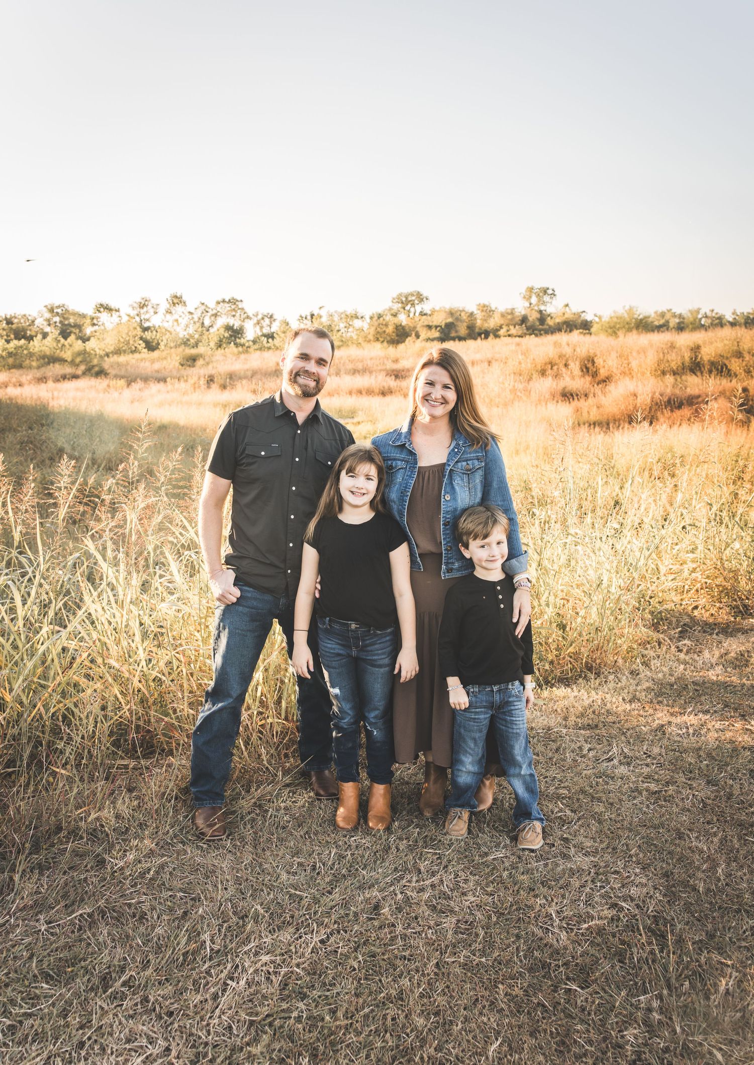 Family poses together in golden autumn field at sunset wearing coordinated casual outfits in earth tones. Missouri City Family Photographer