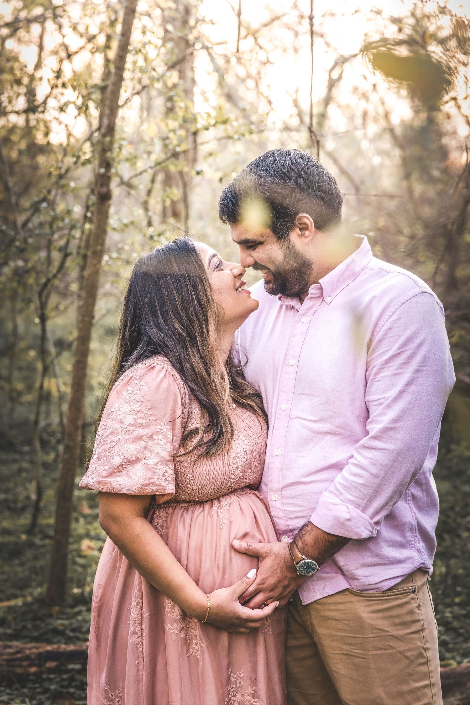 A romantic maternity photo shoot in a sunlit forest with a couple wearing matching pink outfits.  Missouri City Family Photographer