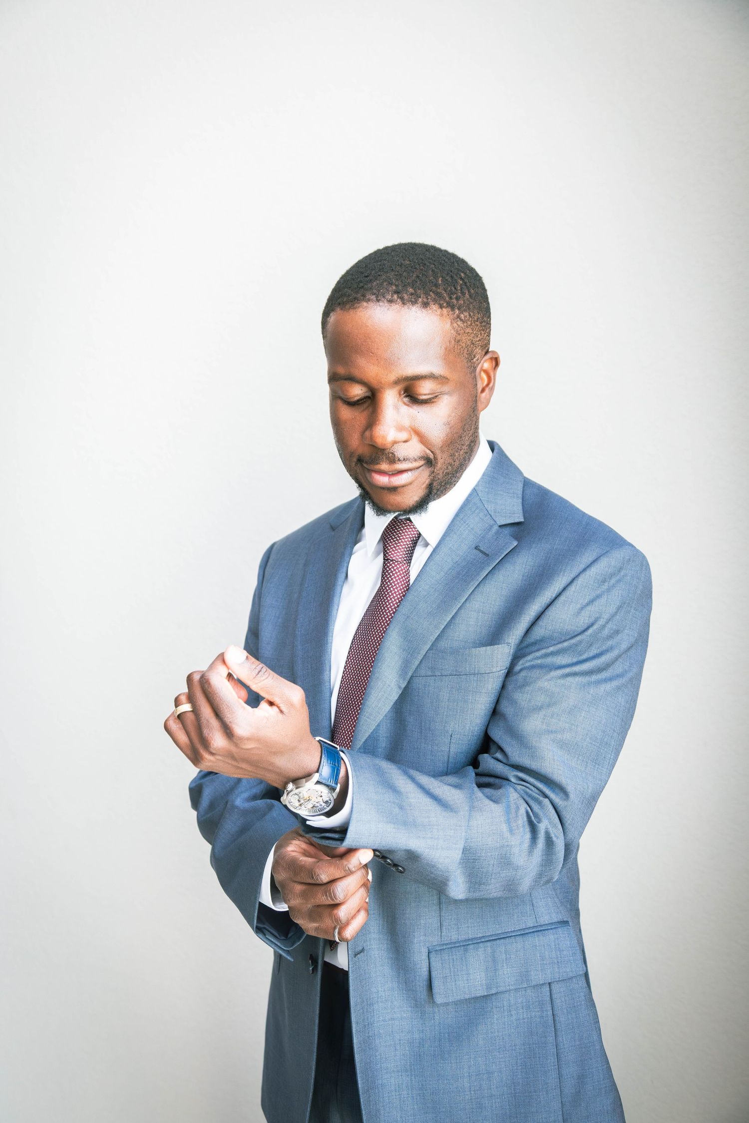 Professional in a light blue suit adjusts his burgundy tie while smiling against a white background.  Missouri City Family Photographer