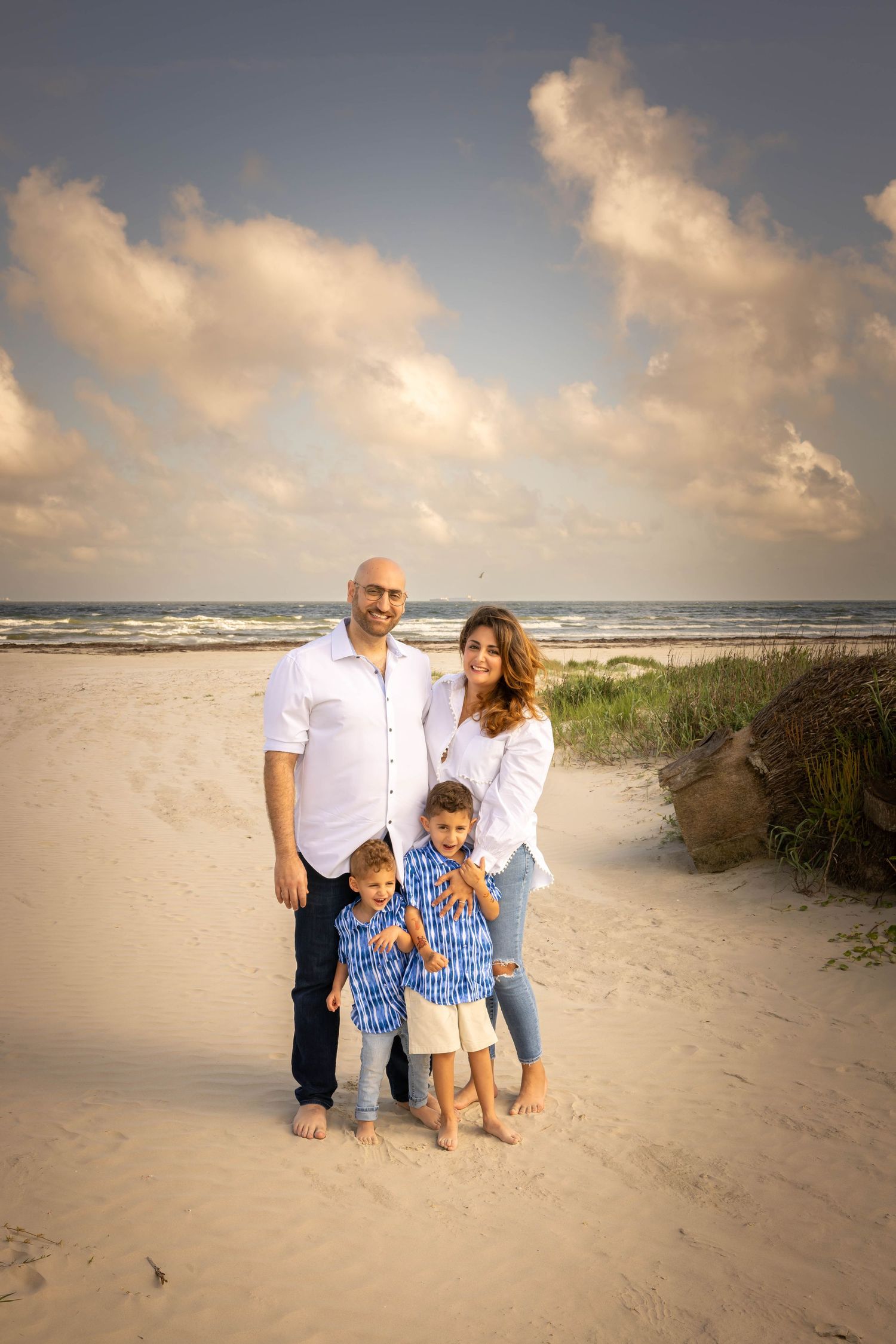 A group enjoys a sunset stroll along a serene beach with sand dunes and ocean waves in the background. Galveston Family Photographer