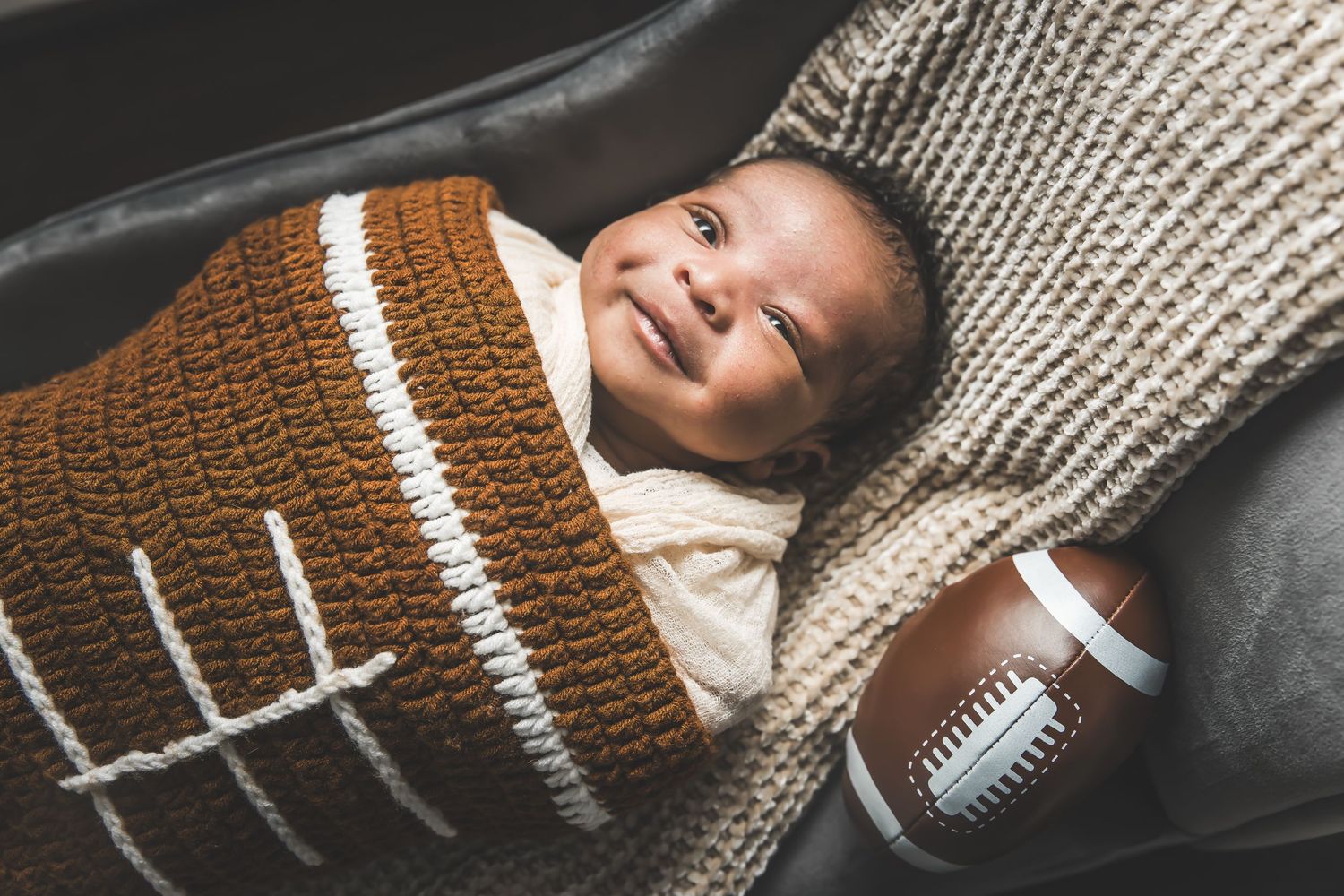 A brown football rests on a dark surface with white stitching details visible in the leather texture.