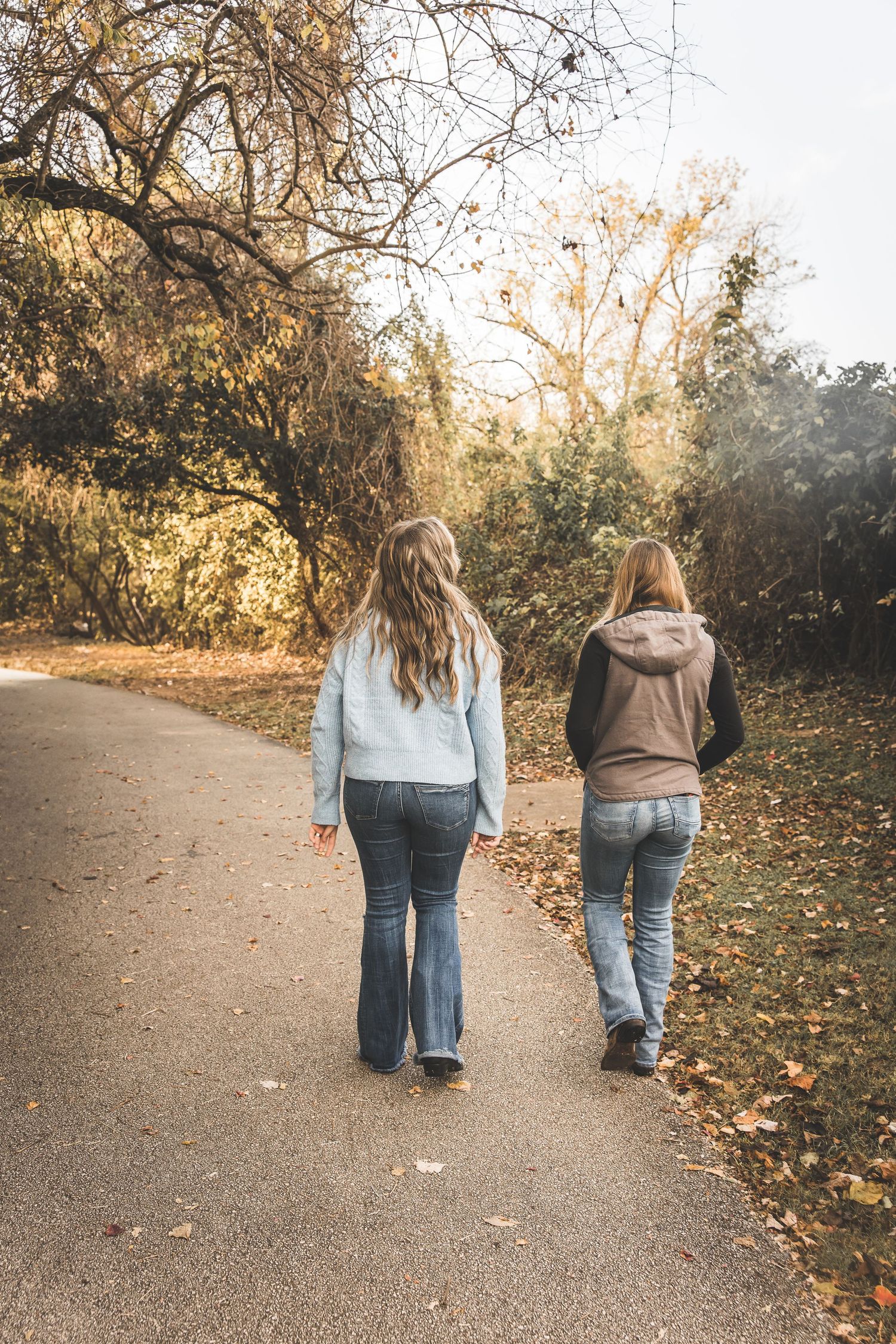 Two people walk together on an autumn path lined with fallen leaves and golden sunlight.  Pearland Family Photographer