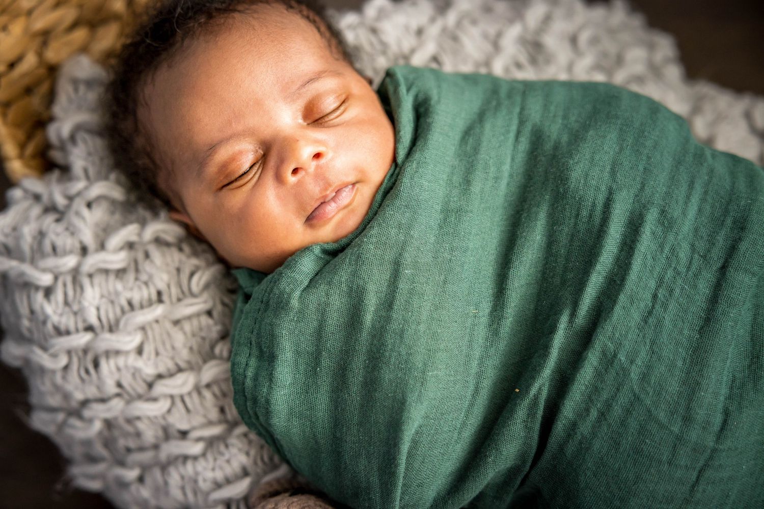 Sleeping newborn baby wrapped in green swaddle blanket rests peacefully on soft gray knit blanket.  Missouri City Family Photographer
