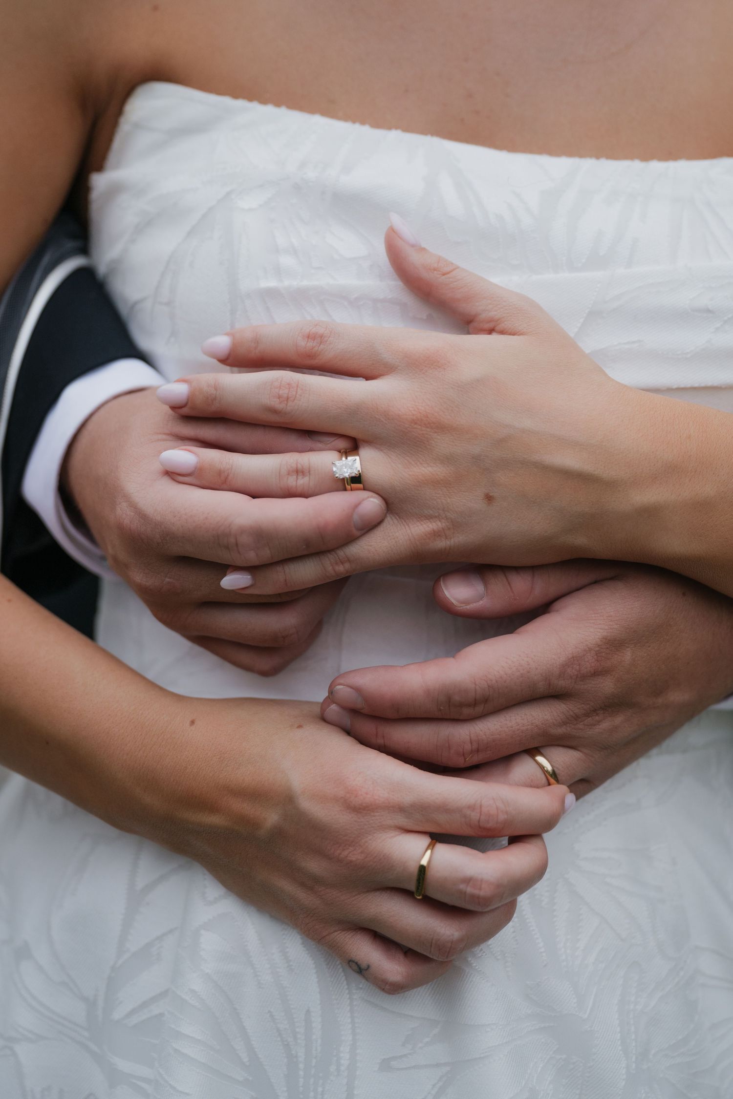 Close-up of newlyweds hands embracing, showing diamond engagement ring and gold wedding bands.