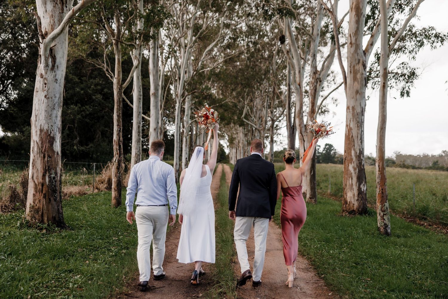 Wedding party walks down a tree-lined path together.