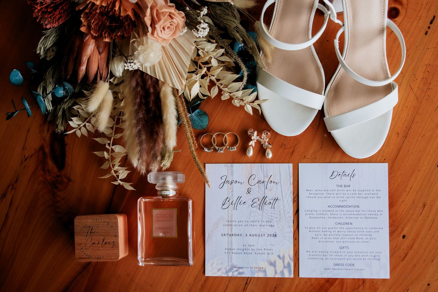 Wedding invitations and decorative details arranged on wooden surface with floral elements.