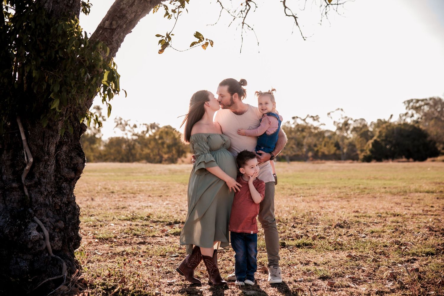 Family shares loving moment together under large tree in golden afternoon light.