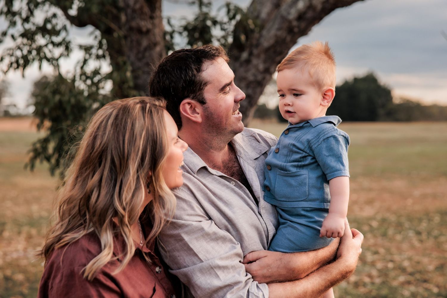 A loving family shares a tender moment together outdoors in a golden field at sunset.