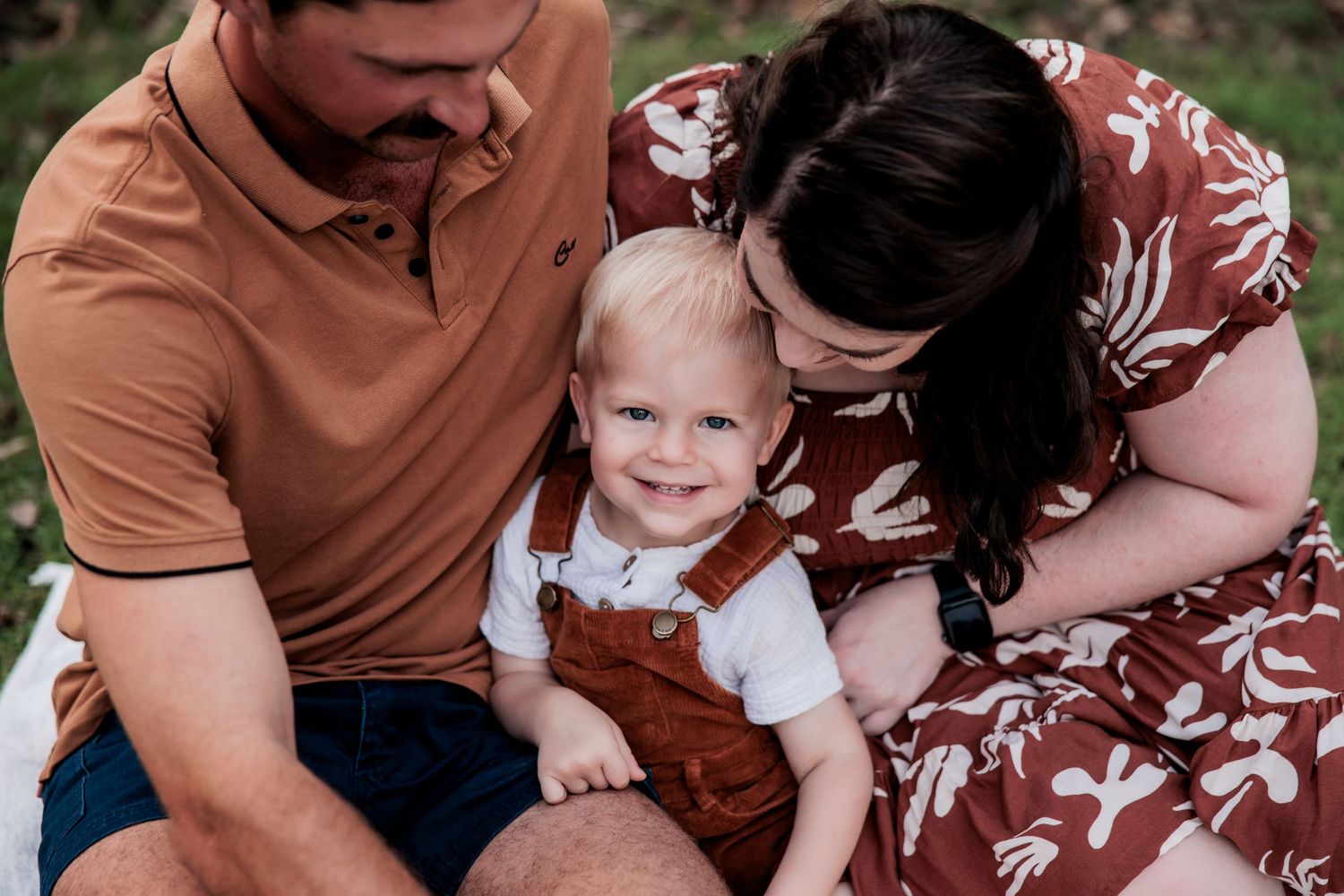 A family sits together on grass wearing coordinated rust and brown tones outdoors.
