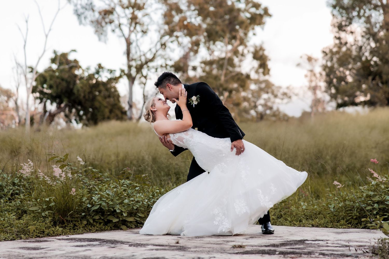 Bride and groom pose playfully on grass during outdoor wedding photography session.