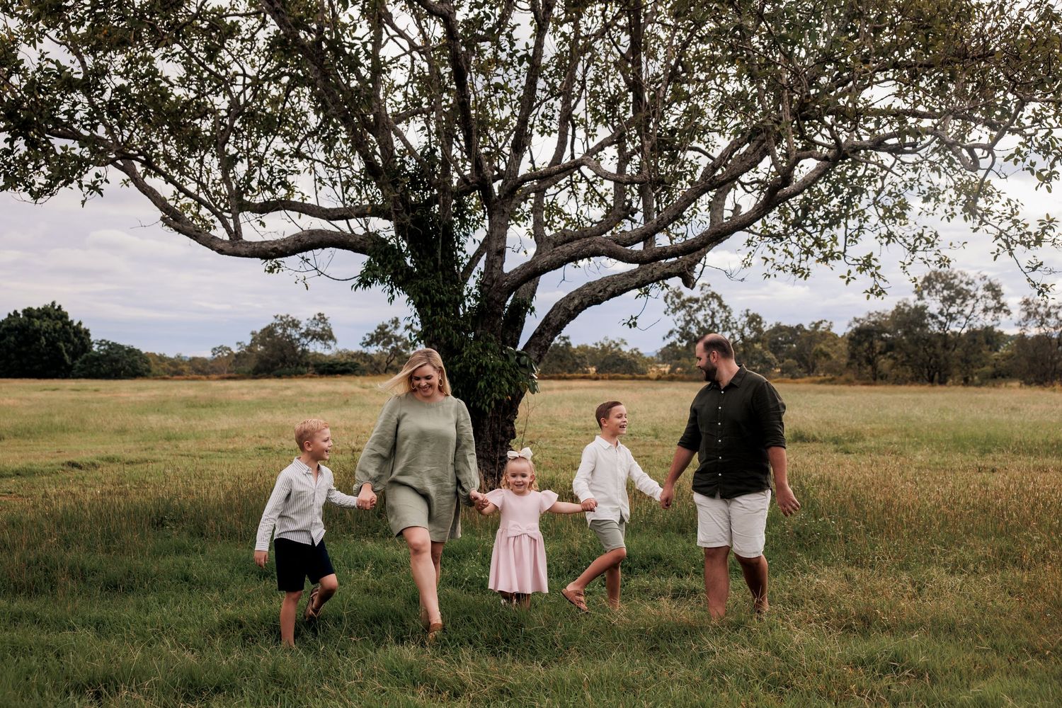 Family members walk hand in hand through a scenic meadow at golden hour, creating silhouettes against the landscape.