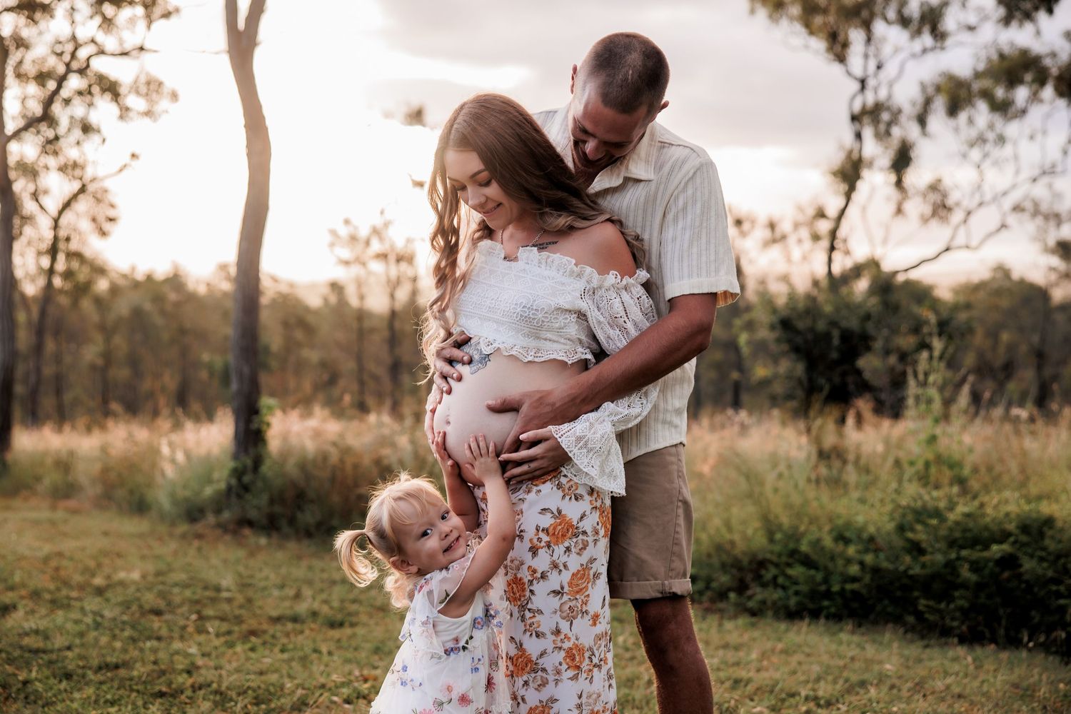 A tender family moment captured in golden light at sunset in a grassy field.