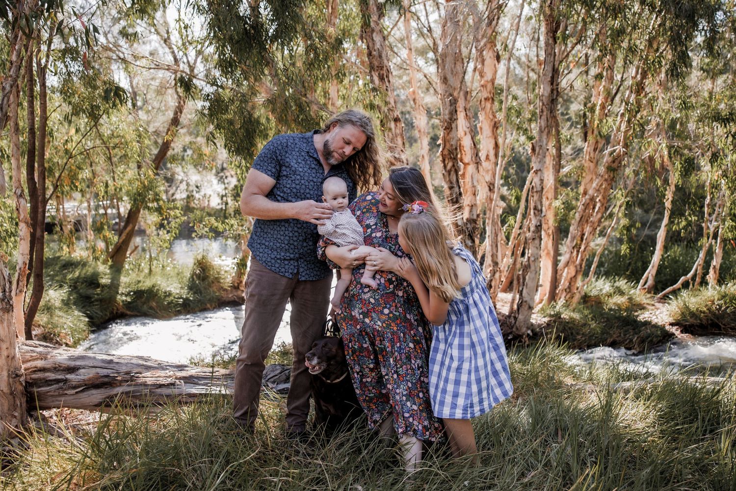 Family enjoys tender moment together outdoors among tall trees.