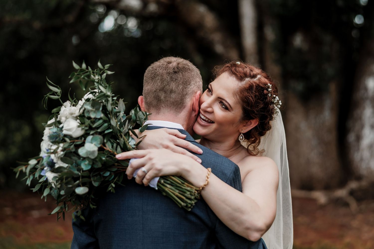 Newlyweds share romantic embraces in a wooded outdoor setting during wedding photoshoot.