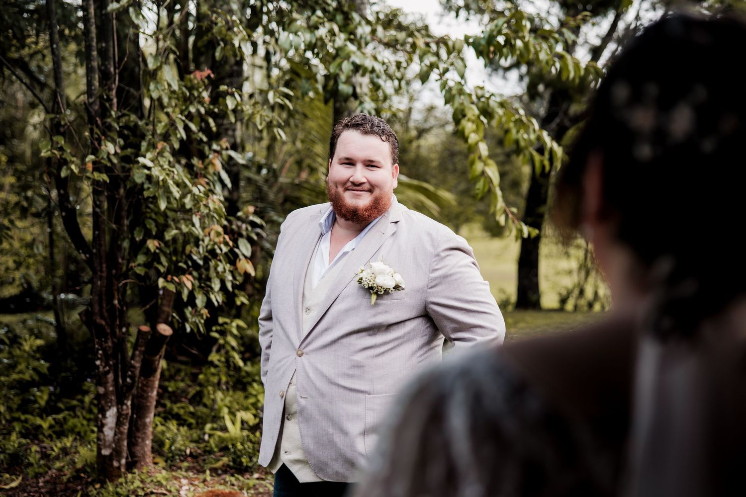 Groom in light gray suit smiling during outdoor wedding photoshoot.