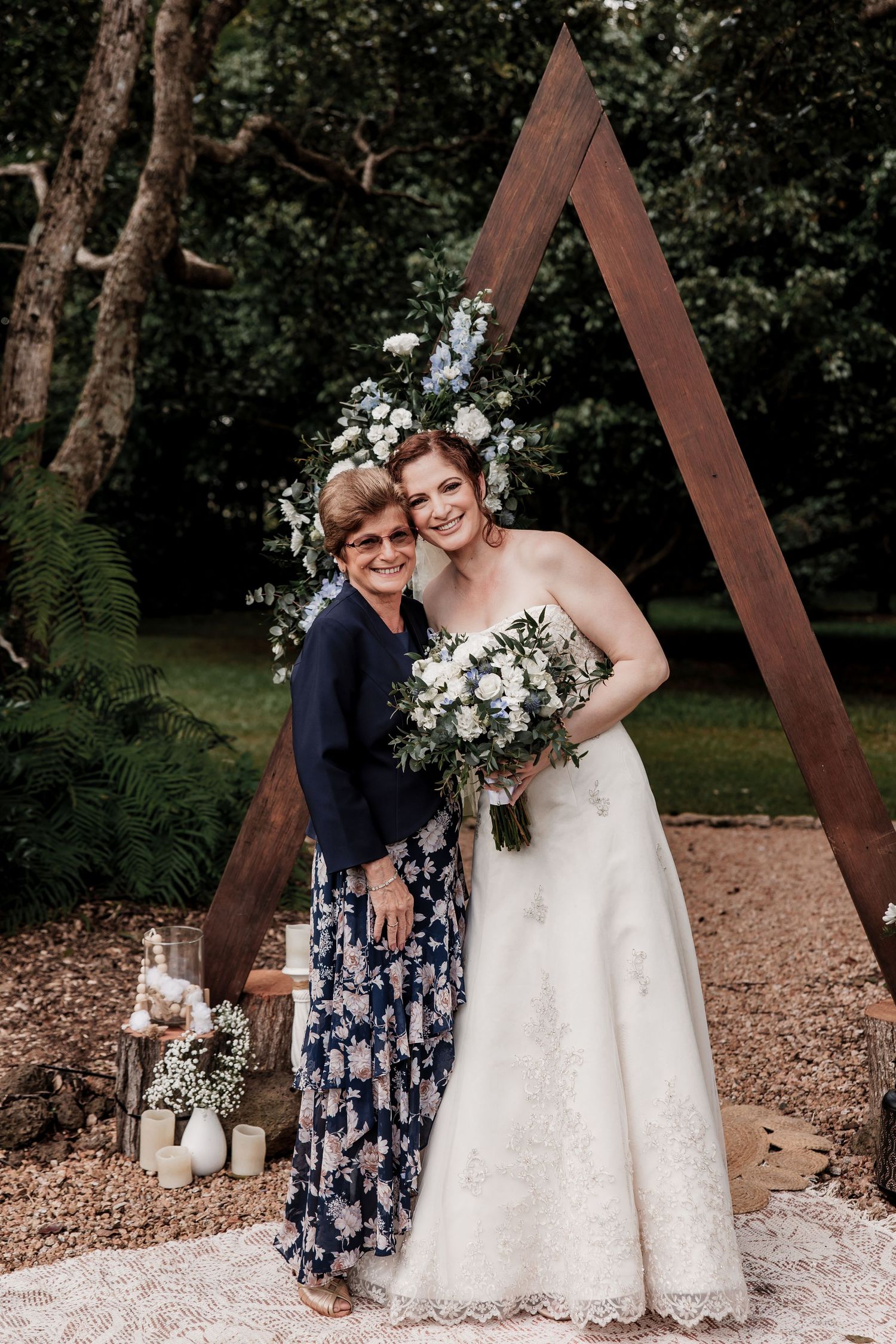 Wedding portrait under a triangular wooden arch decorated with white flowers and greenery.