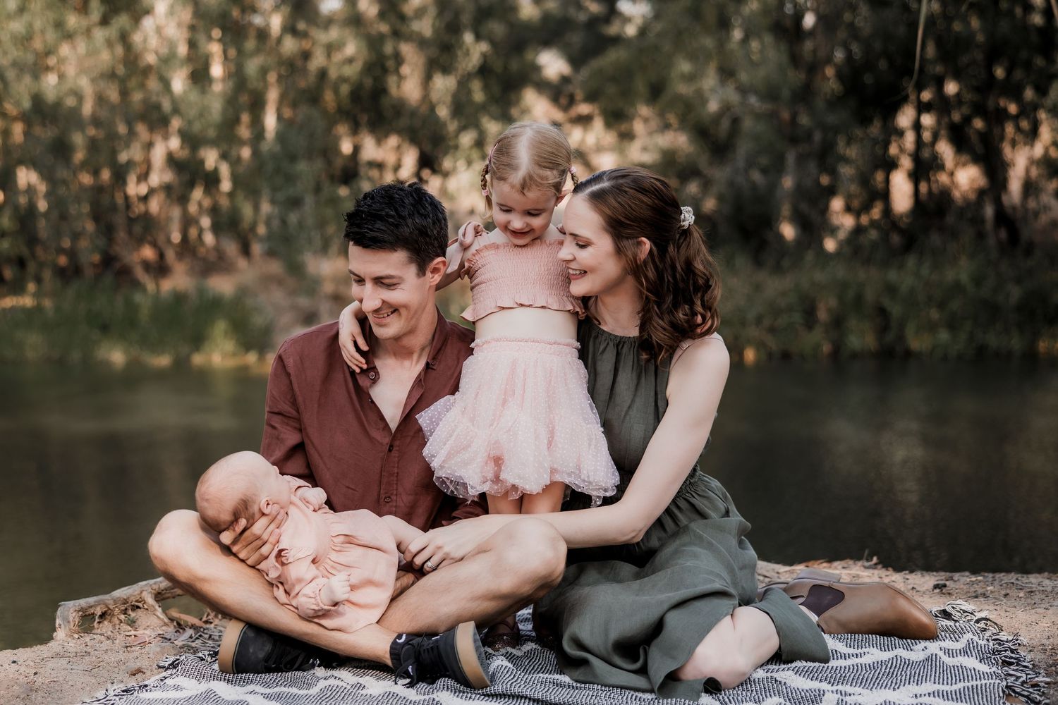 Family shares intimate moment together on rocks by a serene pond.