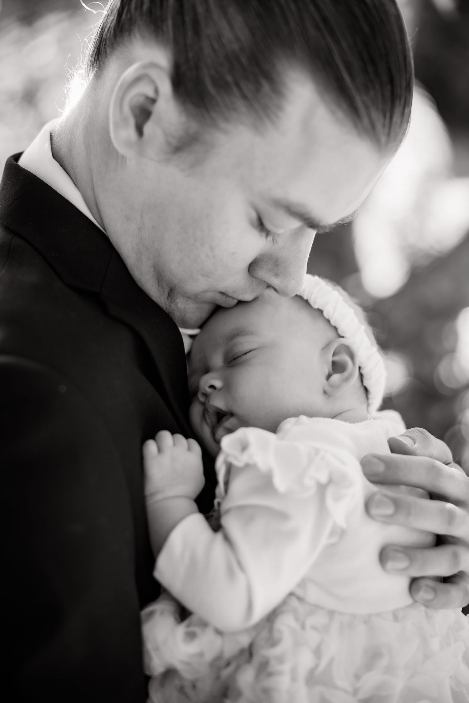Tender black and white portrait of a newborn baby being cradled in formal attire.