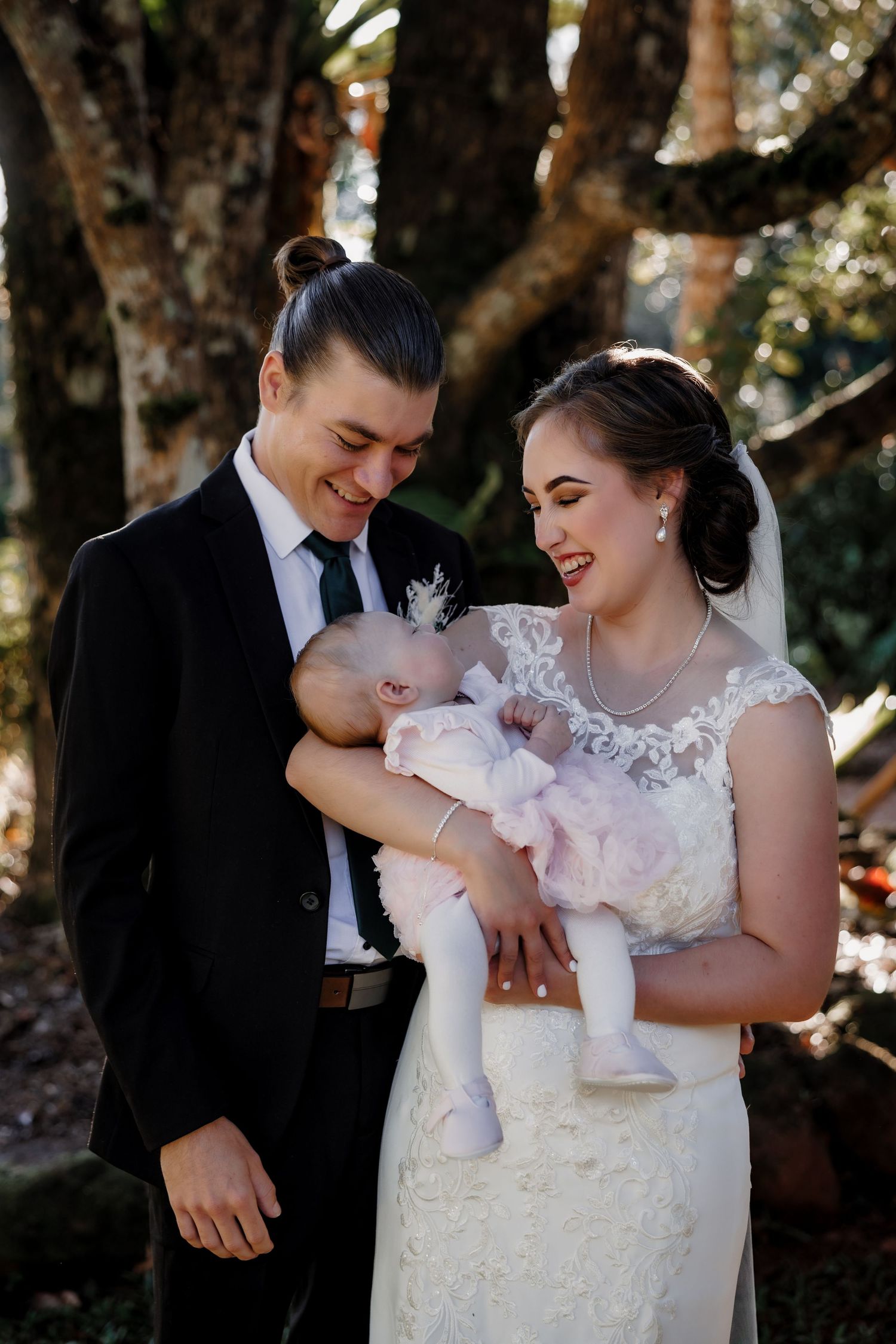 A wedding couple shares a joyful moment with their baby outdoors.