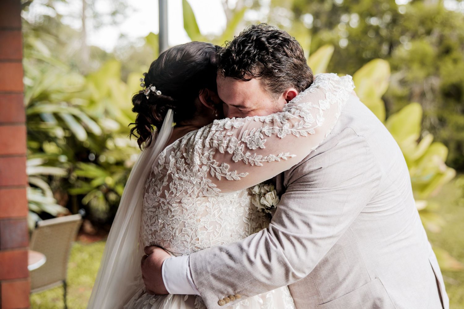 Wedding couple embraces in tender moment surrounded by tropical greenery.