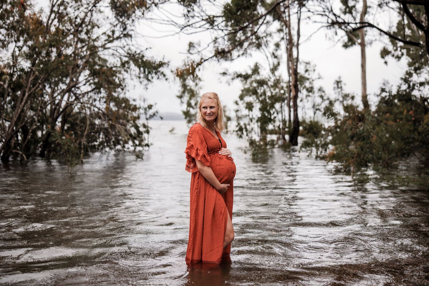 Person in a flowing orange dress standing in flooded waters among tall trees.