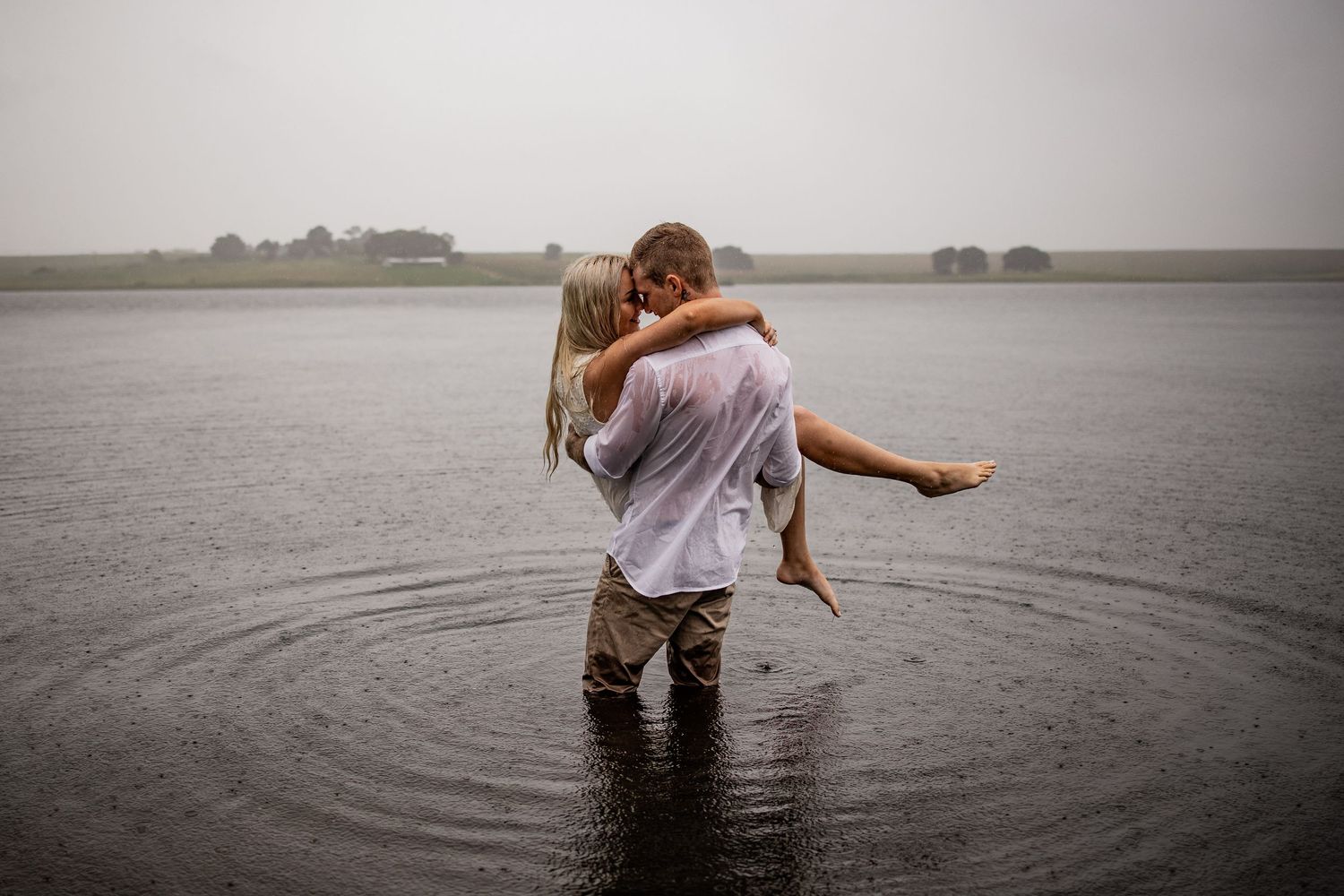 A romantic couple embracing in shallow water on a misty day at the lake.