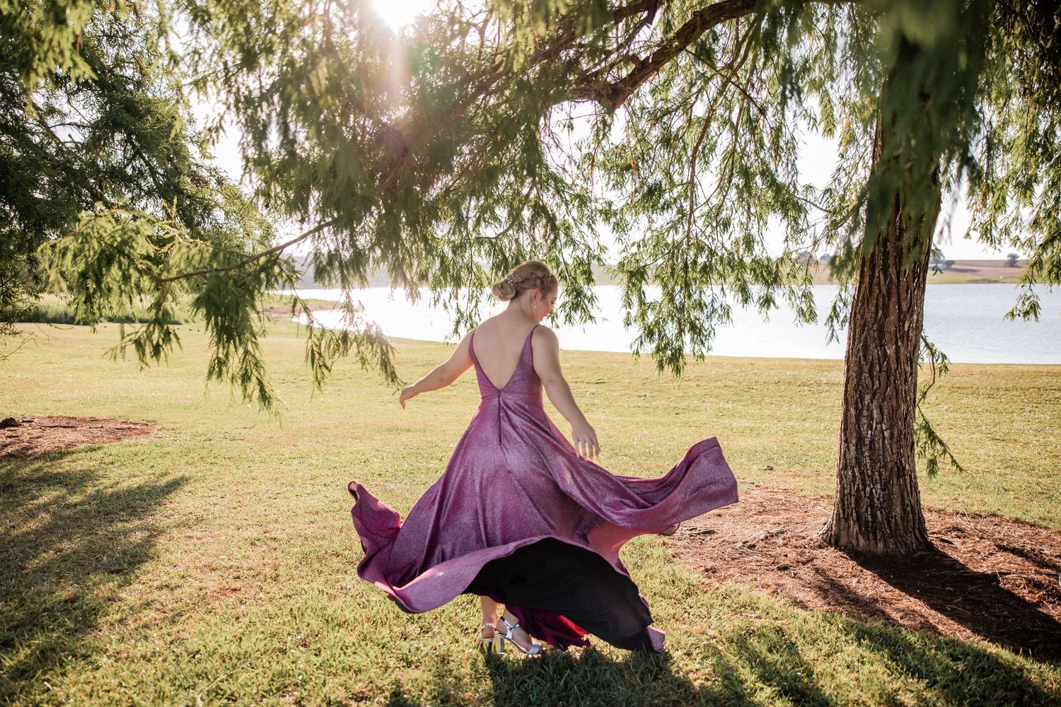 Person in flowing purple dress twirling under tree branches with sunlight peeking through.