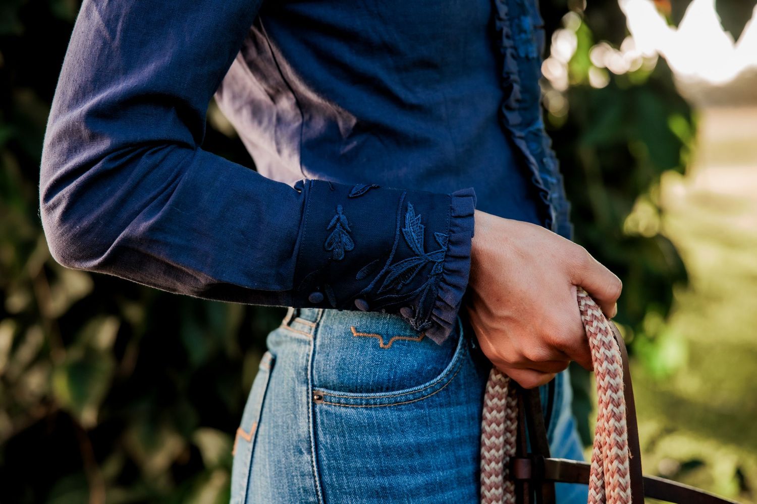 Close-up view of someone wearing blue denim jeans and a navy shirt holding a braided leather handbag strap.