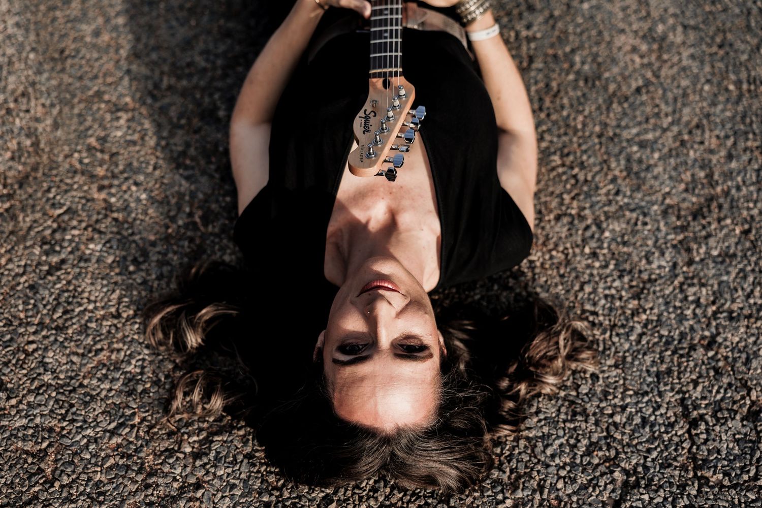 An artistic overhead shot of someone lying on carpet while holding an acoustic guitar neck.