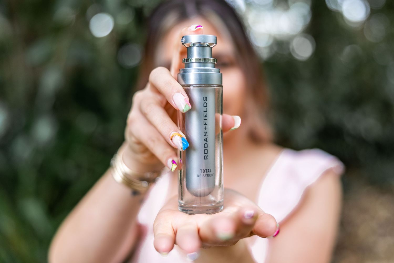 Someone holds up a small glass bottle of serum or essence skincare product against a blurred natural background.