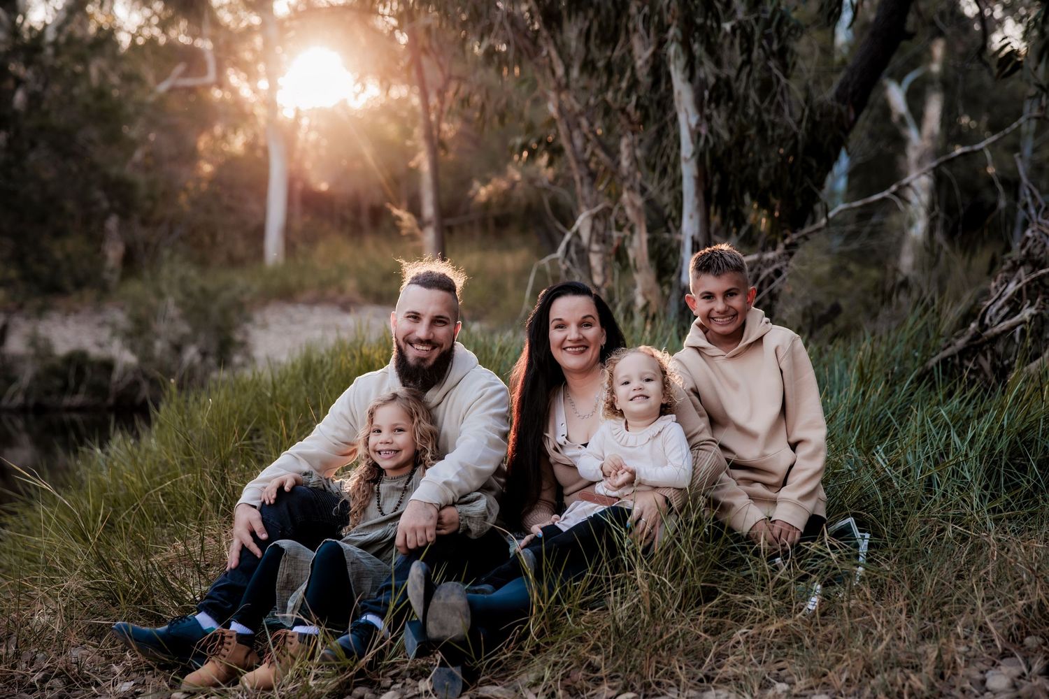 A family of five sits together on grass during golden hour for an outdoor portrait session.