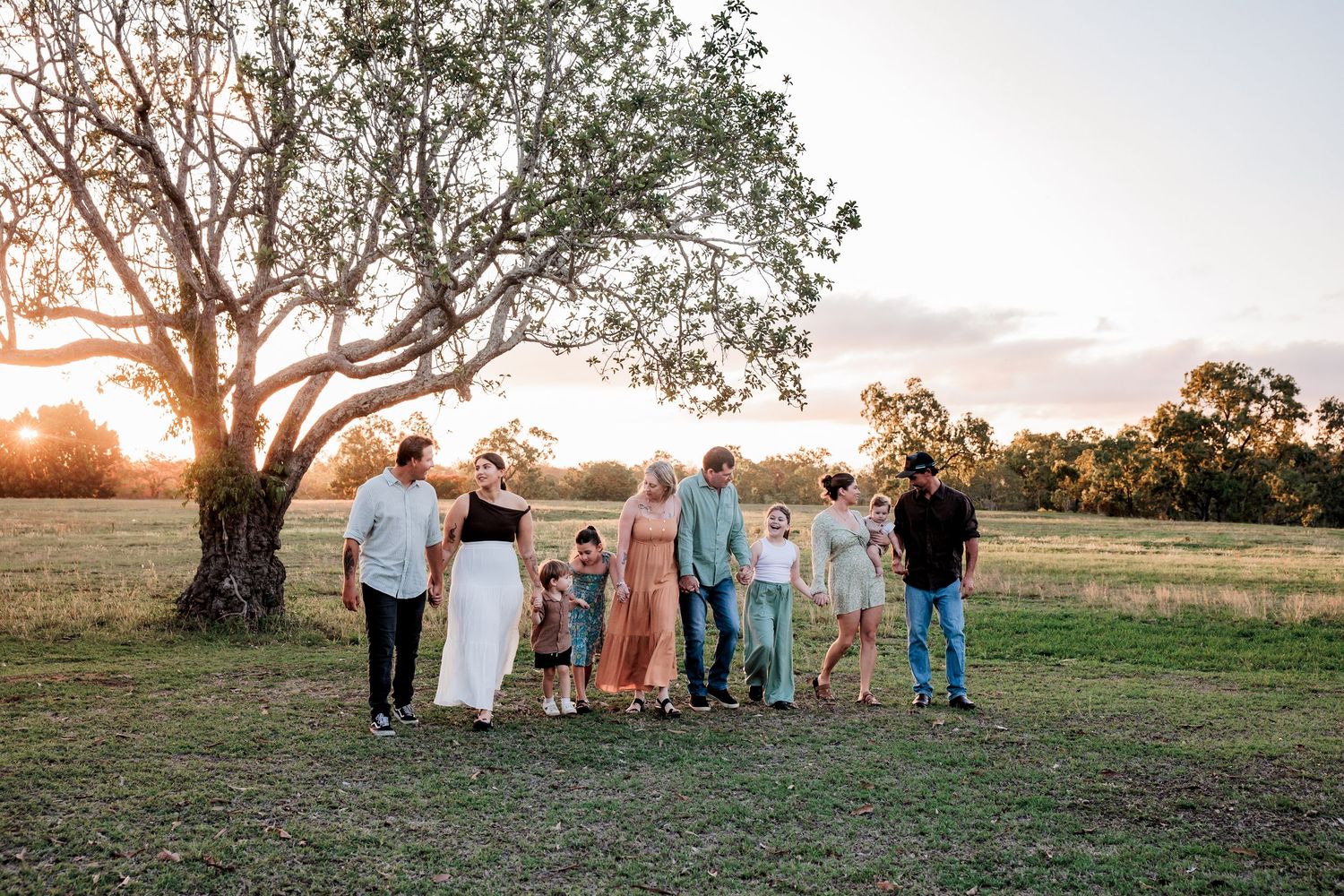 A group stands together on a grassy field at sunset with a large tree silhouetted in the golden evening light.