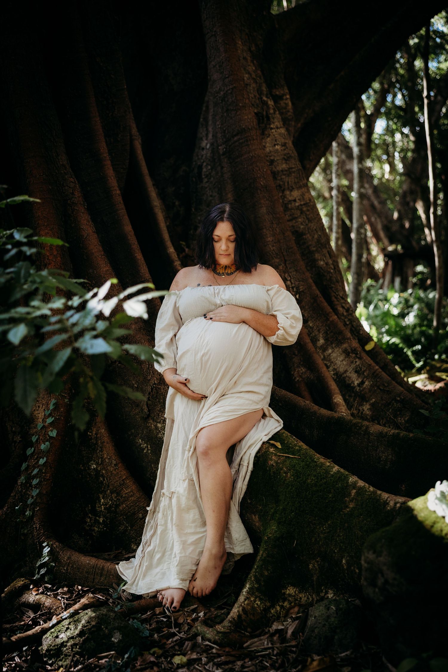 A series of artistic maternity photos taken in a mystical forest setting with large tree roots and natural lighting.