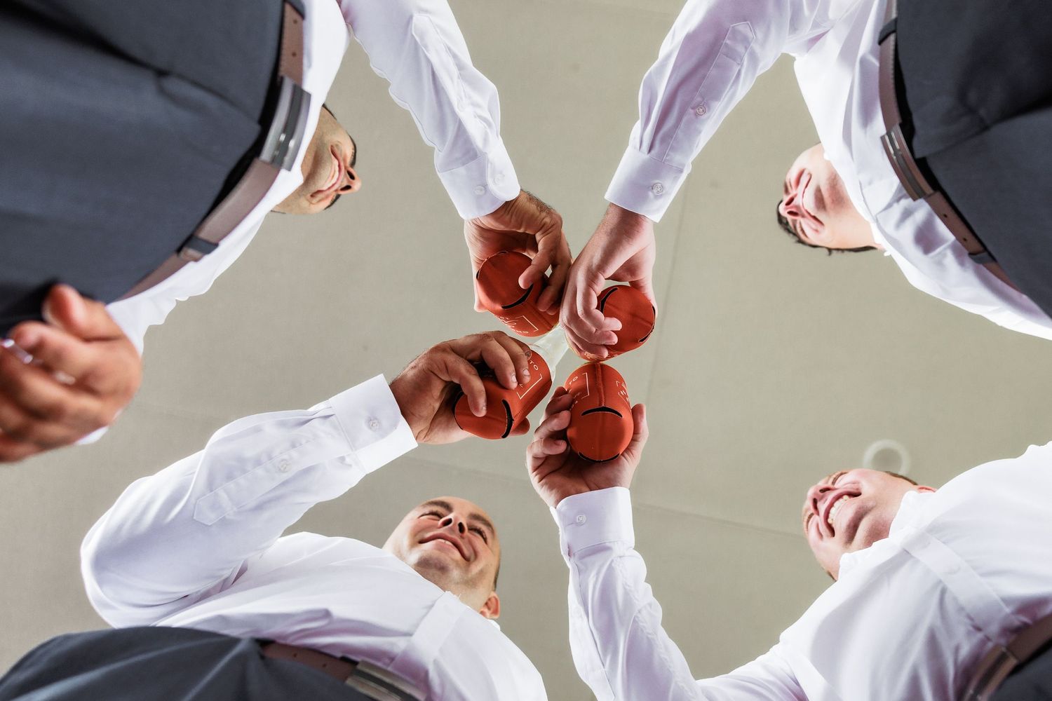Groomsmen toasting with glasses of red wine in a celebratory circle shot from below.