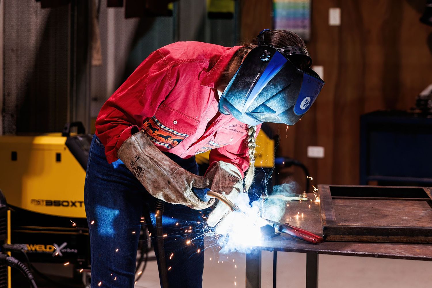 Welders in protective helmets working on a manufacturing line with bright blue welding sparks illuminating the workspace.