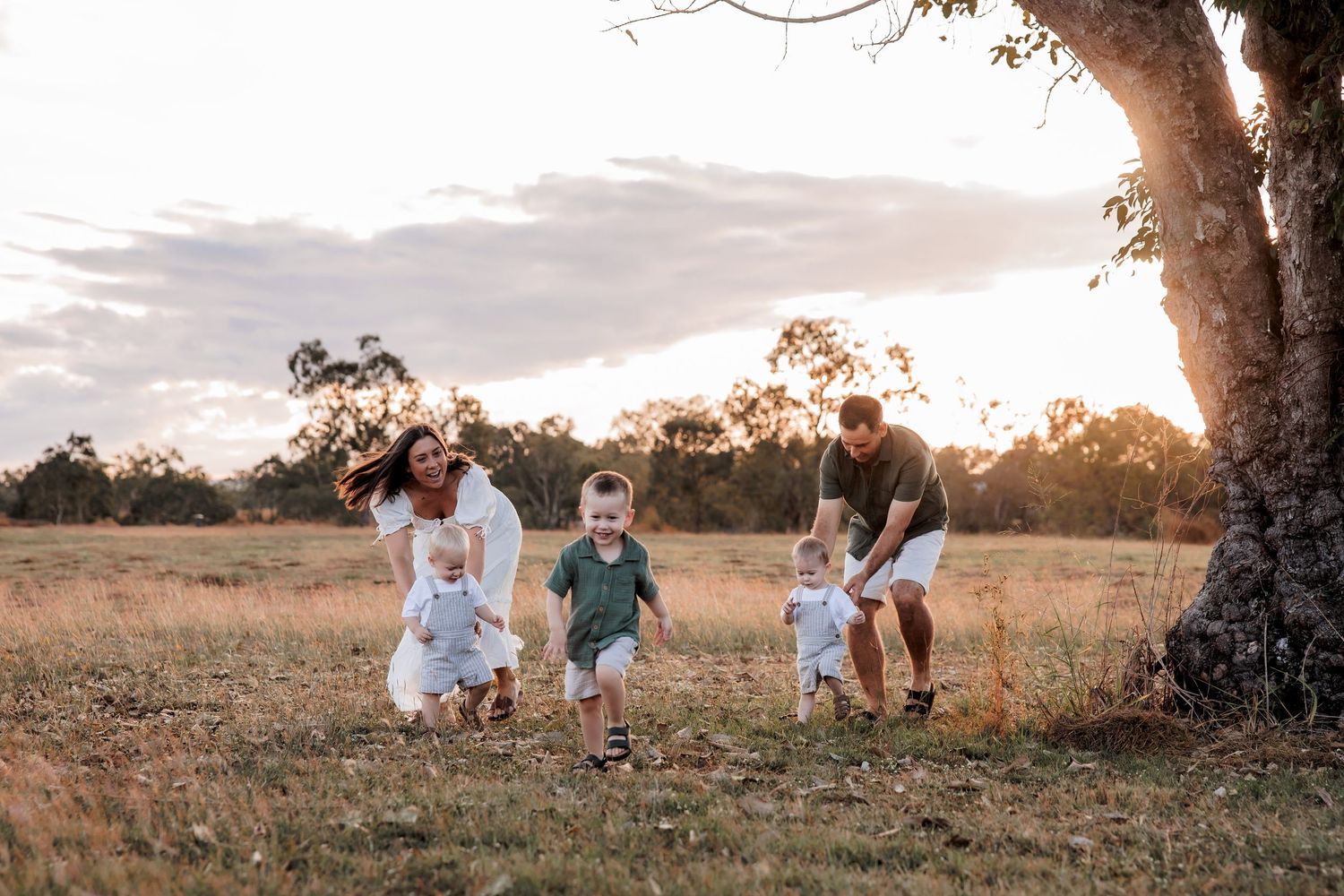 A group playing and running together in a golden field at sunset next to a large tree.