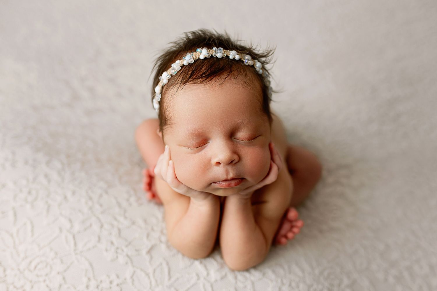 Newborn baby in froggy pose with floral headband on cream textured backdrop at Flowertown Photography newborn studio in Summerville SC